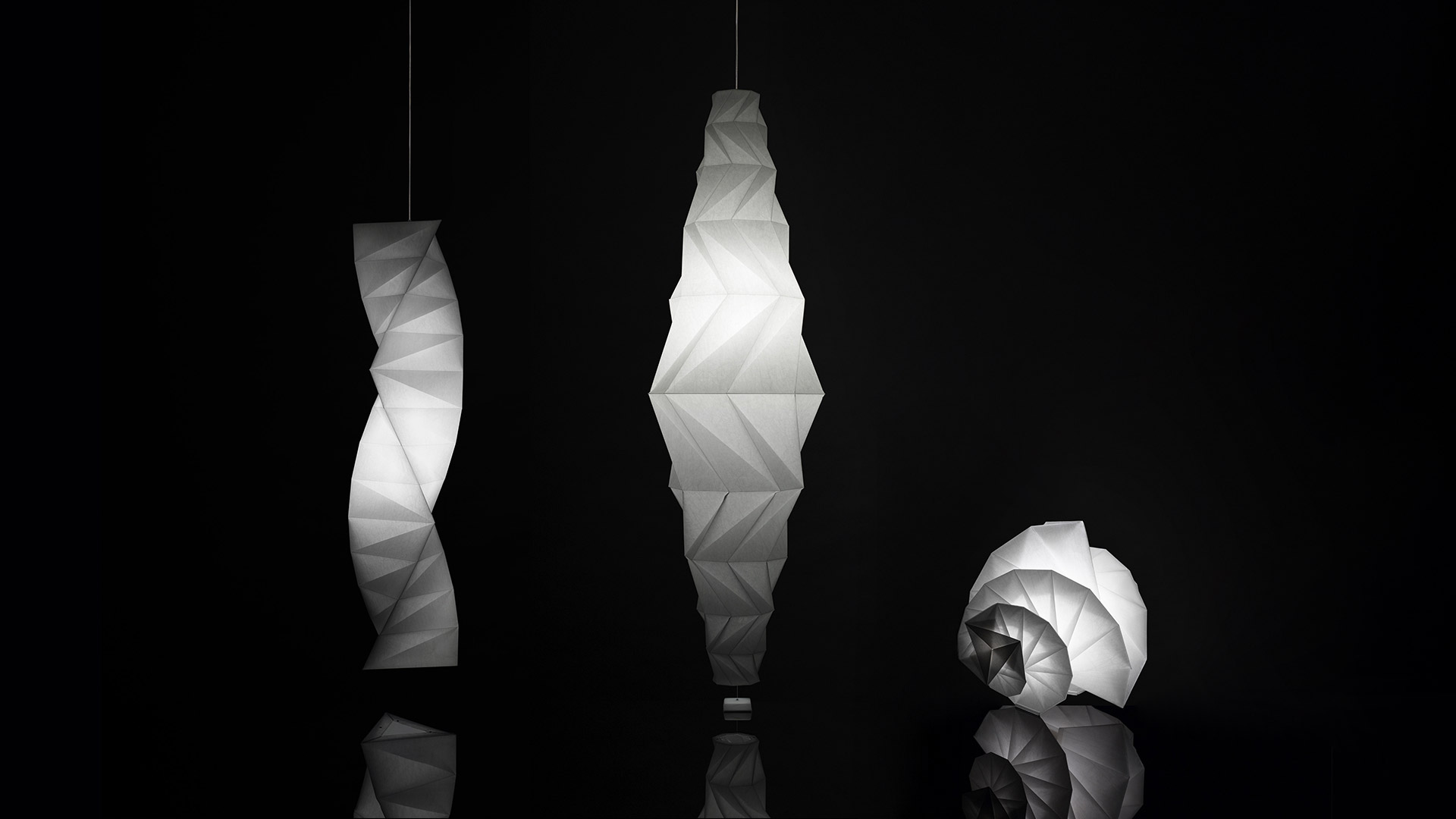 Artemide In-Ei Issey Miyake collection: origami-inspired white pendant and floor lamps with geometric folded shapes in a dimly lit showroom
